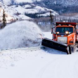 Snow plough truck clearing road after whiteout winter snowstorm blizzard for vehicle access